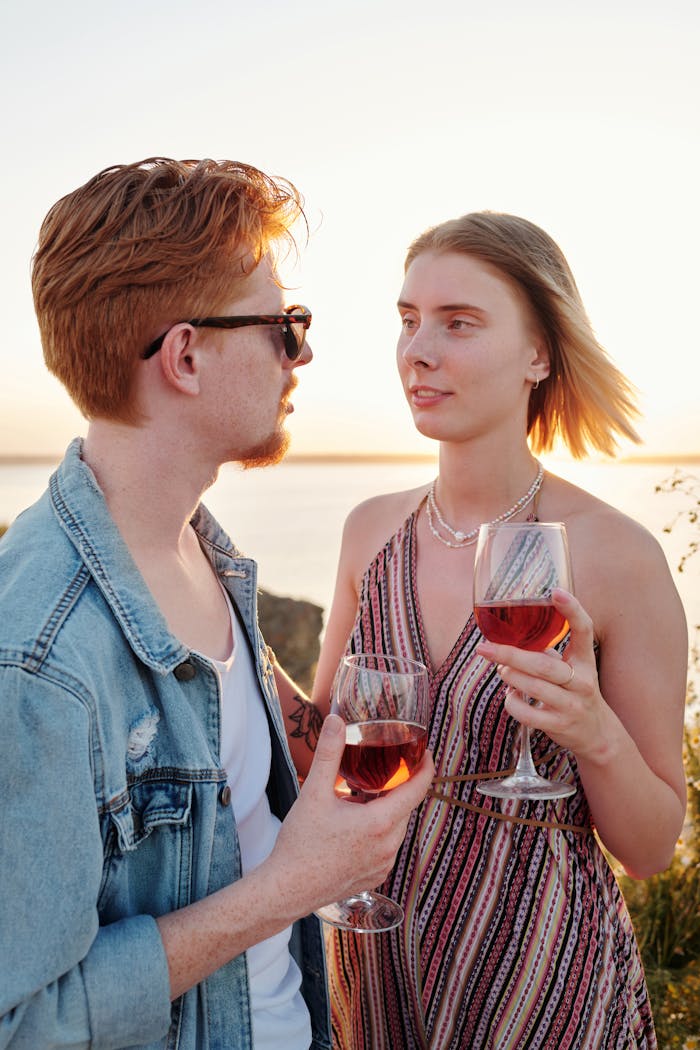 A couple sharing a romantic moment with wine glasses during sunset outdoors.